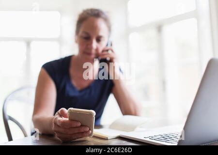 Donna che parla al telefono e usa lo smartphone a casa Foto Stock