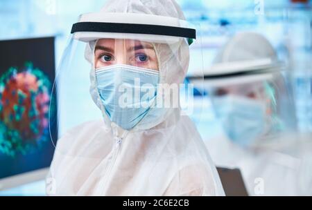 Ritratto sicuro scienziato femminile in tuta pulita studiando coronavirus