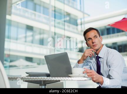 Uomo d'affari pensivo che beve caffè al computer portatile Foto Stock