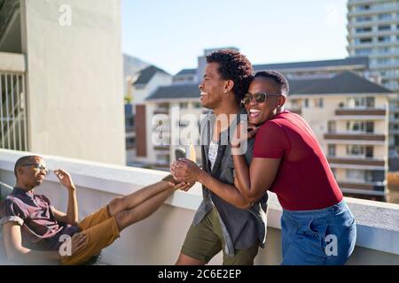 Felice giovane coppia ridendo e abbracciando sul soleggiato balcone urbano Foto Stock