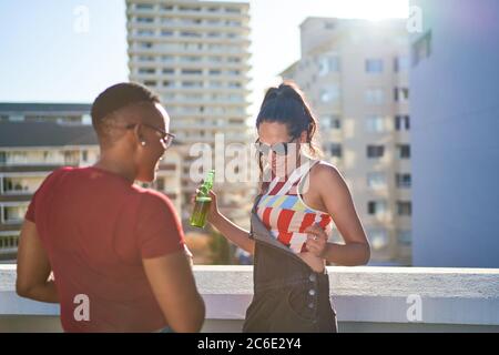 Una giovane donna che danzava e beveva birra sul soleggiato tetto urbano Foto Stock