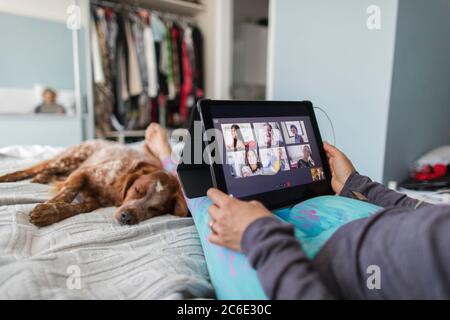 Donna con tablet digitale che parla con gli amici a letto con il cane Foto Stock