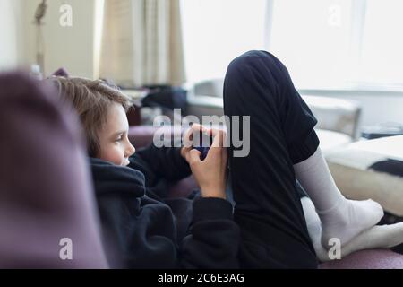 Ragazzo che gioca a un videogioco con smartphone sul divano Foto Stock