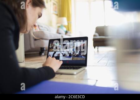 Ragazza adolescente che si esercita in linea a schermo del laptop sul pavimento Foto Stock