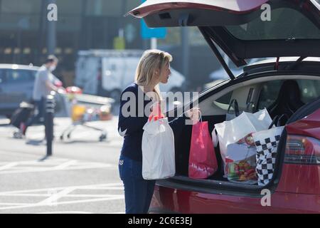 Donna che carica generi alimentari nel retro dell'auto in un parcheggio soleggiato Foto Stock