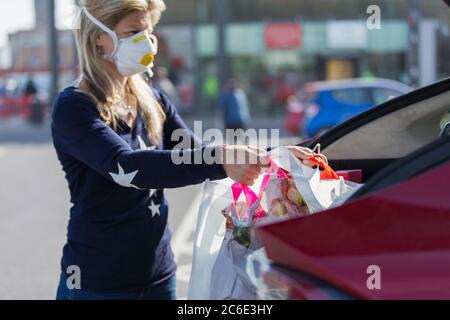 Donna in maschera di faccia caricando gli alimentari in auto Foto Stock