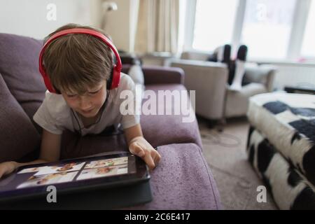 Ragazzo con cuffie e tablet digitale che si trova sul divano Foto Stock