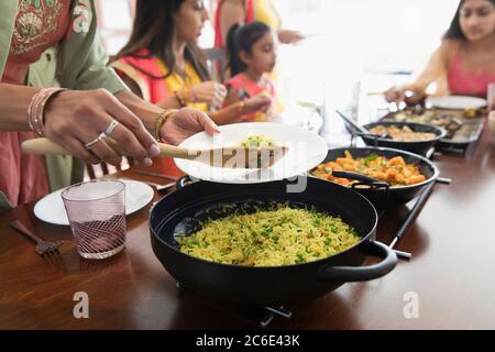 Donne indiane in sari che servono e mangiano cibo a tavola Foto Stock