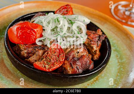 Cucina georgiana. Carne di montone grigliata su spiedini con pomodori al forno e cipolla fresca. Primo piano Foto Stock