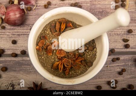 Allspice in un mortaio di ceramica e spicchi d'aglio sparsi, anice stellato e allspice su un tavolo di legno. Primo piano Foto Stock