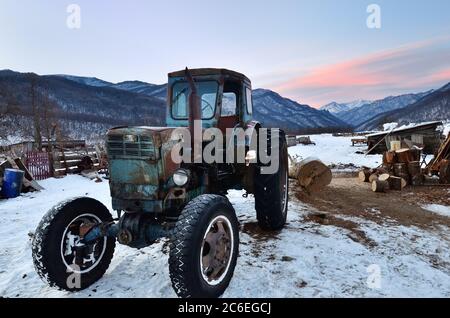 Caucaso, Russia - 18 febbraio 2012: Vecchio trattore sovietico arrugginito mostrato su casa colonica cortile in villaggio in montagna regione del Caucaso montagna all'alba i Foto Stock