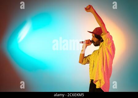 Movimento. Giovane musicista ispirato ed espressivo, cantante che suona su sfondo sfumato colorato in luce al neon. Concetto di musica, hobby, festival, artista gioioso, colorato, ritratto luminoso. Foto Stock