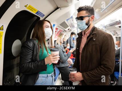 Pendolari che indossano maschere sulla metropolitana di Londra. Treno Jubilee Line. Coppia che va a fare shopping nel West End. 6 luglio 2020. Londra, Regno Unito. CONSE Foto Stock