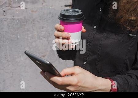 Ragazza con tazza da caffè tiene lo smartphone in mano da vicino Foto Stock