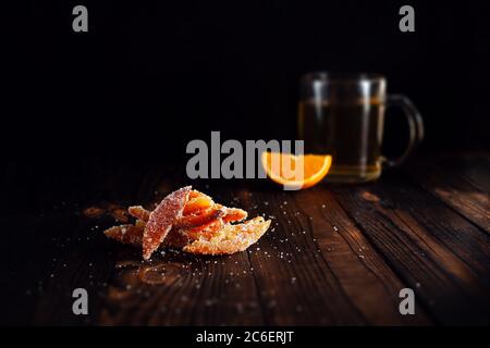 Bucce di arancia nello zucchero. Frutta candita di arancio. Marmellata d'arancia su un tavolo marrone di legno con fondo nero. Tè con arancia a fette. Vuoto Foto Stock