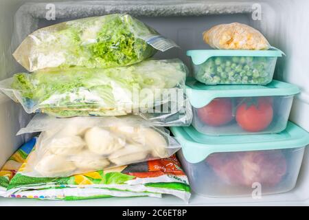 Verdure e carne surgelate in contenitori di plastica blu. Mais giallo congelato, piselli verdi, pomodori rossi, carne, gnocchi, verdure miste, insalata. Foto Stock