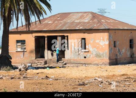 Casa vecchia, decrepita, trascurata con un uomo africano in piedi fuori mostrando povertà e condizioni di vita povere nella città di Città del Capo, Sud Africa Foto Stock