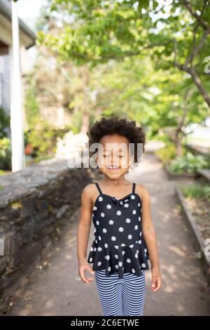 Giovane bella ragazza afroamericana in piedi in ambiente urbano con un'espressione carina, candida e felice. Foto Stock