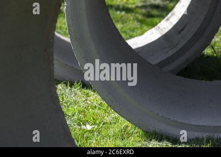 Anelli massicci di calcestruzzo sono adagati su erba verde, sfondo astratto industriale foto Foto Stock