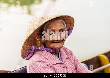 Vecchia donna vietnamita in felpa viola e cappello è seduta su una barca mentre sorride Foto Stock