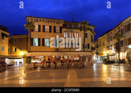 Scena notturna nel centro storico di Sirmione, in particolare la vivace atmosfera di Piazza Carducci con i suoi numerosi ristoranti. Sirmione è un co Foto Stock