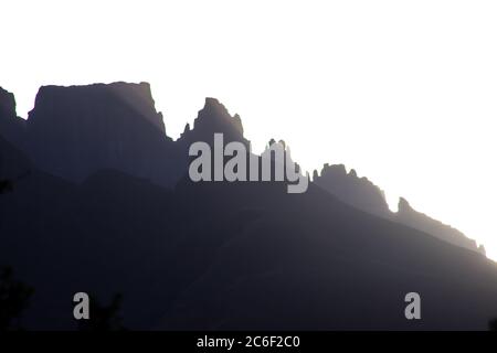 Gli ultimi raggi del sole che tramonta attraverso i Pinnacoli del Dragons Back, una delle montagne iconiche dei monti Drakensberg nel sud Foto Stock