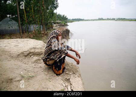 Manikganj. 9 luglio 2020. Una donna si siede sulla riva accanto al sito dove la sua casa è stata lavata via lungo un fiume nel distretto di Manikganj, circa 63 km a nord-ovest della capitale Dhaka, Bangladesh, 9 luglio 2020. Le inondazioni causate da forti piogge e dall'afflusso di acqua dalle colline hanno gravemente colpito gli abitanti del villaggio. Credit: Xinhua/Alamy Live News Foto Stock