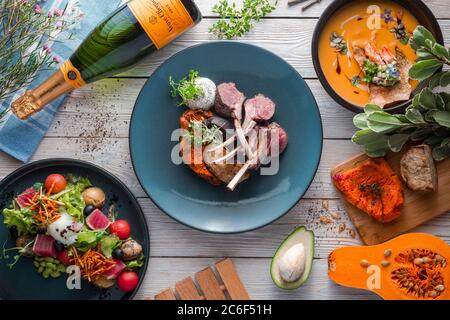 Succosa rack di un giovane agnello con zuppa di zucca e zucca panna su un tavolo bianco. Il ristorante serve dallo chef. Sfondo di legno. Vista dall'alto. Disposizione piatta Foto Stock