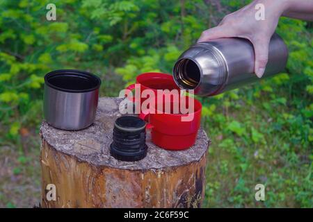 La mano della donna versa il tè caldo fuori dei thermos sullo sfondo della foresta estiva. Foto Stock