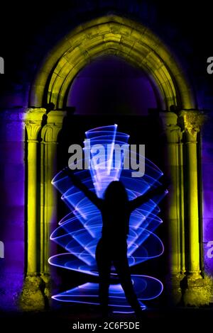 Silhouette di una donna in sessione di pittura leggera. Scultura in stile gotico con arco. Forma astratta curva con fuoco bengala. Foto Stock