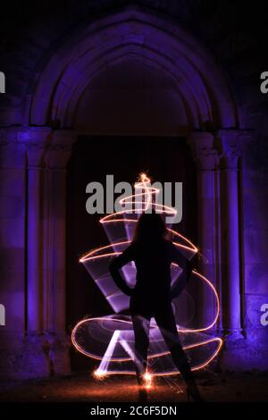 Silhouette di una donna in sessione di pittura leggera. Scultura in stile gotico con arco. Forma astratta curva con fuoco bengala. Foto Stock