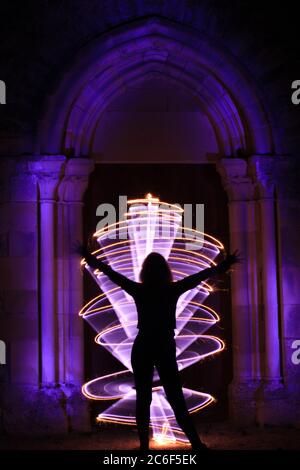 Silhouette di una donna in sessione di pittura leggera. Scultura in stile gotico con arco. Forma astratta curva con fuoco bengala. Foto Stock