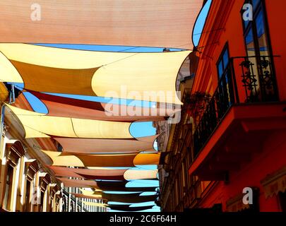 Tenda e tenda avvolti in tessuto colorato e avvolti da sole vele UV, sospesi dall'esterno sopra la strada urbana. Zona centro storico. protezione solare Foto Stock