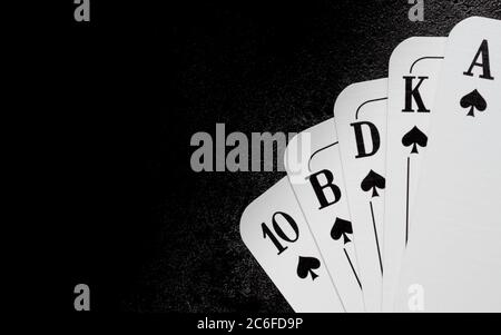 cinque carte da gioco bianche di picche formano un filo reale nell'angolo inferiore destro sulla superficie di ghisa nera con spazio di copia sul lato sinistro Foto Stock