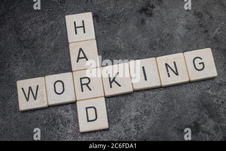 piastrelle di legno per lettere che formano parole su una superficie di ghisa grigia sullo sfondo, lavorando sodo Foto Stock