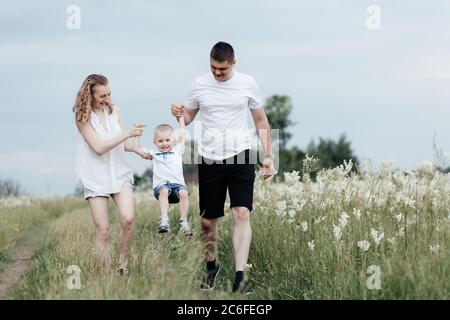 Il momento di sollevare il figlio tenendo le mani da mamma felice e papà mentre cammina sulla natura. Famiglia giovane e felice. Madre, padre e figliolo Foto Stock