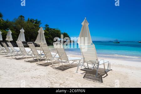 un gruppo di sedie da spiaggia vuote invitanti a prendere il sole in una spiaggia bianca di fronte alle acque cristalline dei caraibi Foto Stock