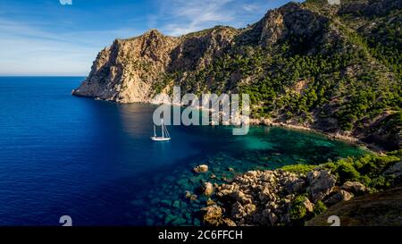 vista da torre de cala en basset su una barca a vela bianca a due alberi che si aggira in una piccola baia idilliaca sul crinale della trappa vicino a sant elm Foto Stock