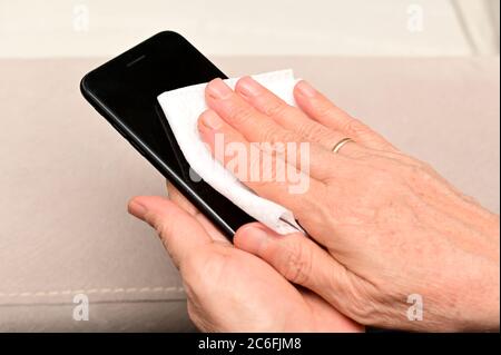 La donna anziana sta pulendo lo schermo del suo smartphone per eliminare i germi, covid-19 con l'alcool. Foto Stock