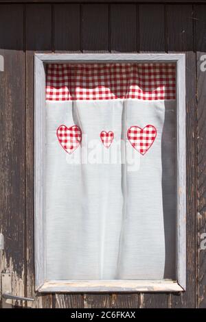Tenda finestra con forme rosse del cuore su una casa in legno chalet nella regione delle Alpi Foto Stock