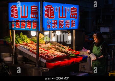 Taipei, Taiwan - 24 dicembre 2018: Una signora sta per preparare il pesce per gli ospiti al mercato notturno di Guangzhou Street nel quartiere più antico di Taipei, Wanhua. Foto Stock