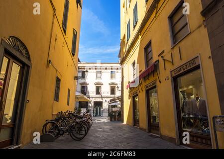 Lucca, Italia - 17 agosto 2019: Fila di biciclette parcheggiate nella stretta strada con caffè e negozi nel centro storico di Lucca, Toscana Foto Stock