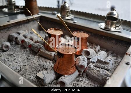 Preparazione tradizionale del caffè turco in pentole di rame su carboni ardenti Foto Stock