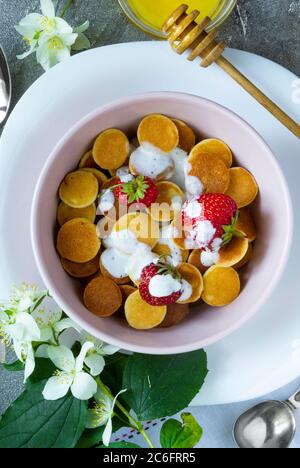 Cibo alla moda - cereali pancake. Un mucchio di mini frittelle di cereali con fragole e yogurt in un boul leggero. Vista dall'alto o in piano. Foto Stock