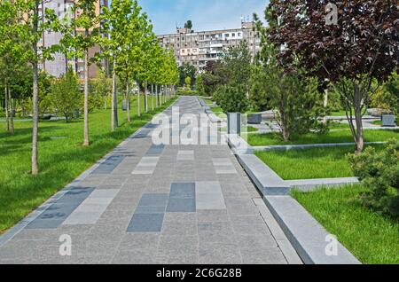 Sentiero pedonale rivestito di granito nel parco cittadino vicino a edifici residenziali in una calda giornata estiva Foto Stock