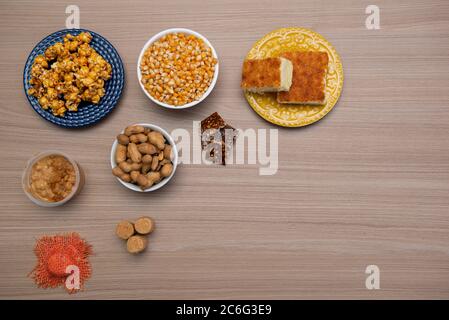 Vista dall'alto dei tipici cibi di giugno Party su un tavolo di legno: Popcorn, torta di farina di mais, noccioline, caramelle di arachidi (paçoca) e dulce de leche Foto Stock