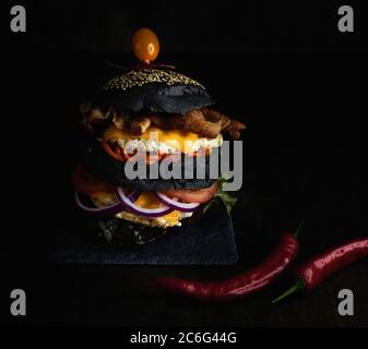 Hamburger nero con doppio polpettine di pollo e doppio formaggio, pancetta e carote su un asse di pietra. Foto di alta qualità Foto Stock