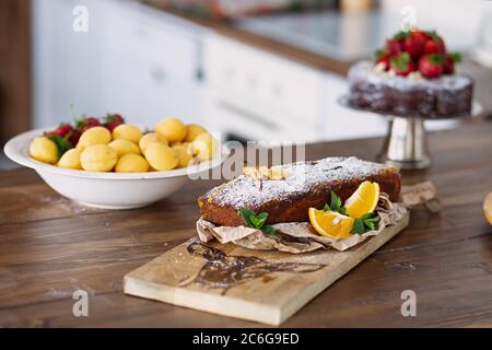 la torta di carote si trova su tavola di legno, il cibo è decorato con fette di arancia e menta, in un piatto accanto a loro albicocche e al cioccolato torus con fragbe Foto Stock