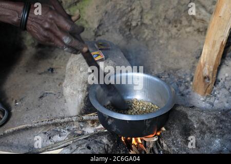 Donna che prepara il caffè sul fuoco, arrostendo i chicchi di caffè, Uganda Foto Stock