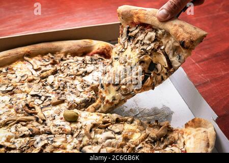 Mano dell'uomo che prende la pizza in una scatola di cartone. Concetto di consegna di cibo, primo piano. Foto Stock